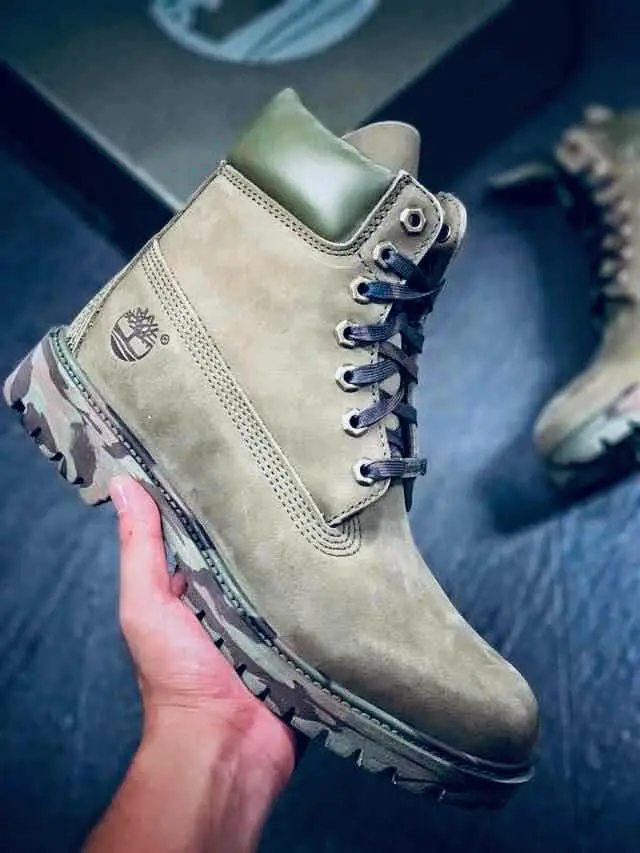 Bottine montante beige avec col vert et semelle camouflage, tenue à la main sur un fond sombre.