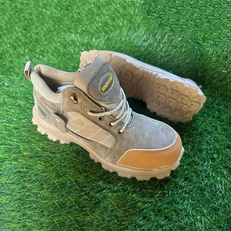 Chaussures de sécurité basses beiges avec renfort orange au bout, semelle crantée beige clair, posées sur du gazon synthétique.