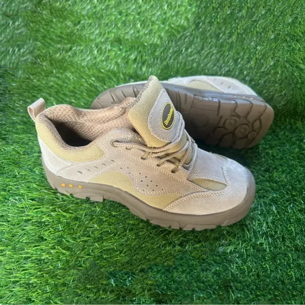 Chaussures de sécurité basses beige clair avec semelle marron et design aéré, posées sur du gazon synthétique.