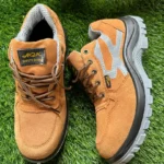 Paire de chaussures de sécurité marron clair avec semelle grise et doublure intérieure en maille, posée sur un gazon synthétique.