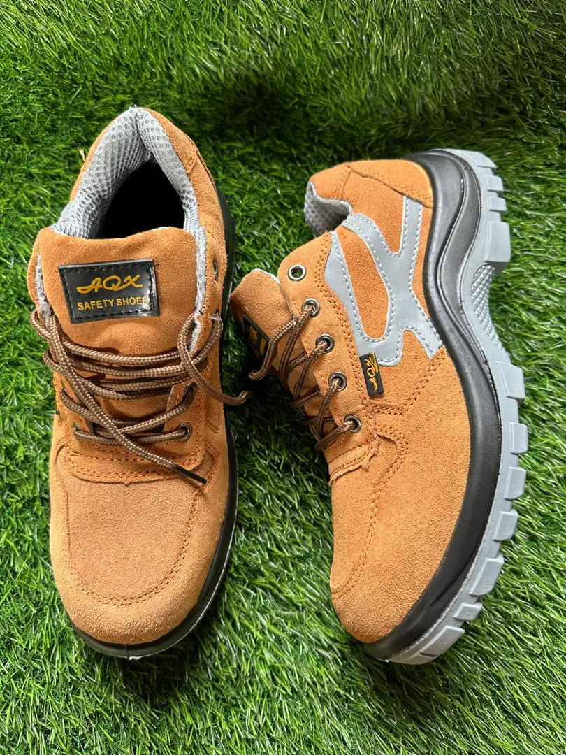 Paire de chaussures de sécurité marron clair avec semelle grise et doublure intérieure en maille, posée sur un gazon synthétique.