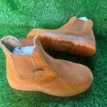 Chaussures de sécurité montantes marron clair sans lacets, posées sur du gazon synthétique.