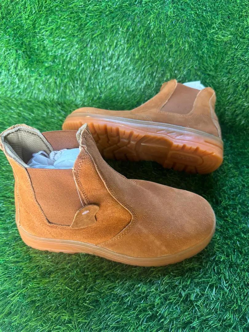 Chaussures de sécurité montantes marron clair sans lacets, posées sur du gazon synthétique.