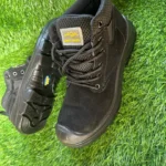 Chaussures de sécurité montantes noires avec embout renforcé et maille respirante, posées sur un gazon synthétique.