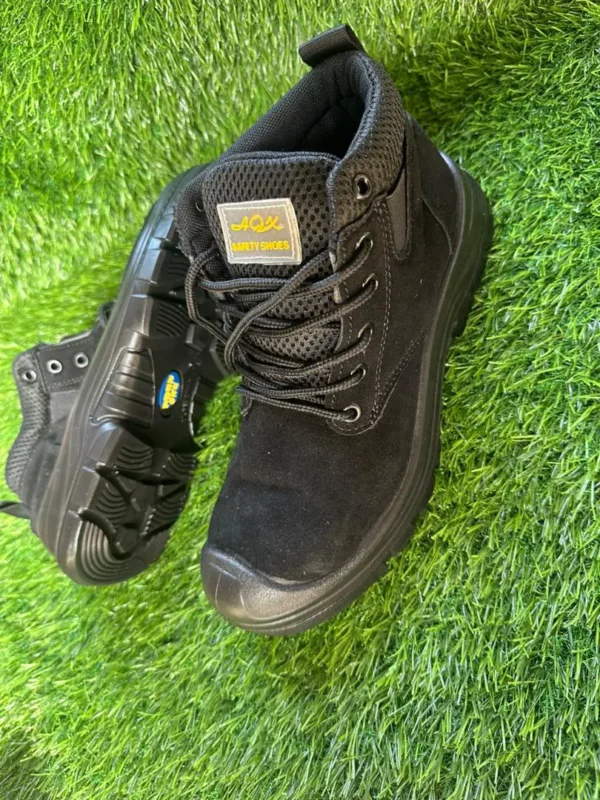 Chaussures de sécurité montantes – noires, confort renforcé Chaussures de sécurité montantes noires avec embout renforcé et maille respirante, posées sur un gazon synthétique.