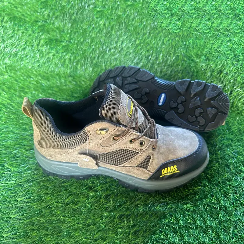 Chaussures de sécurité basses couleur taupe avec semelle noire crantée, posées sur du gazon synthétique.