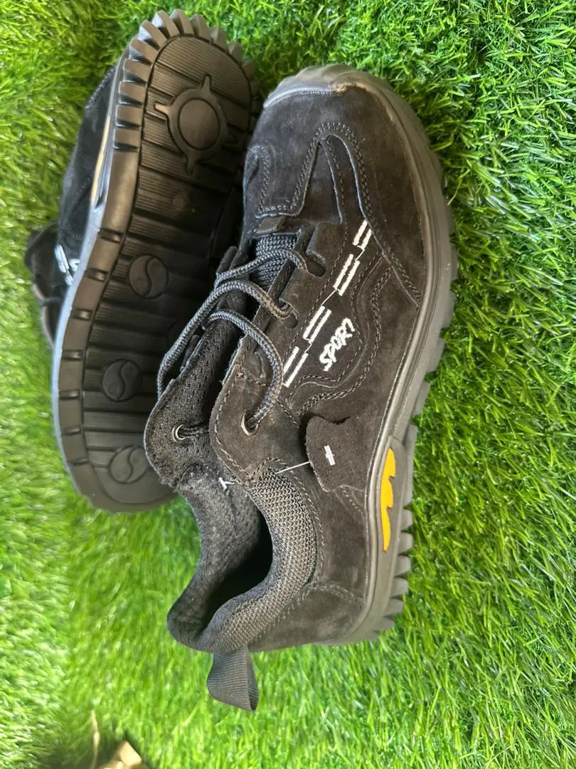 Chaussures noires de type sport avec semelle crantée robuste, posées sur du gazon synthétique.