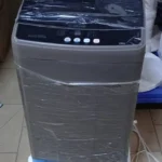 Machine à laver automatique de type top avec panneau de contrôle numérique et couvercle transparent.
